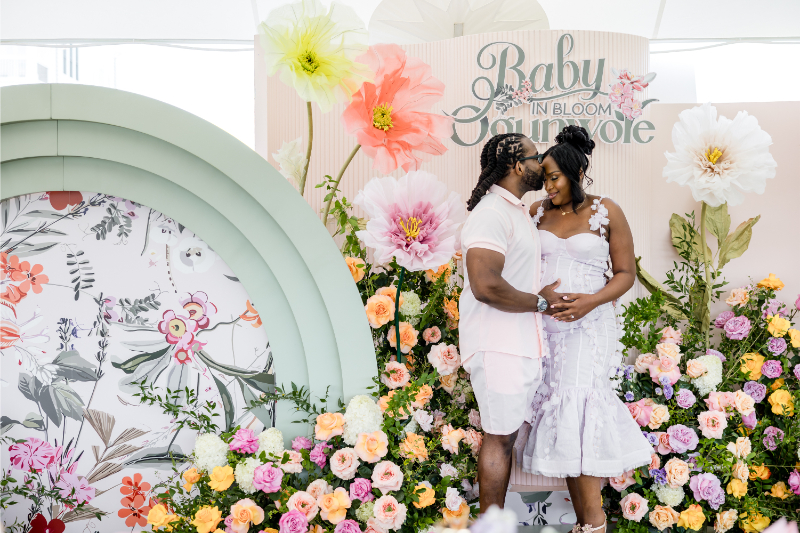 Mother-to-be and father pose in front of custom signage at their colorful baby shower.