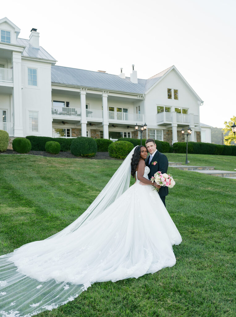 Bride and groom stand on lawn at the View of Bluemont, with the view of their mansion wedding venue behind them.