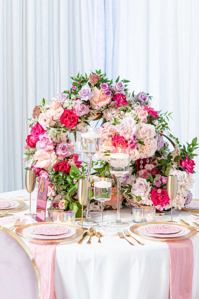 Circular flower covered bridal shower centerpieces with clear candle holders in front of it.