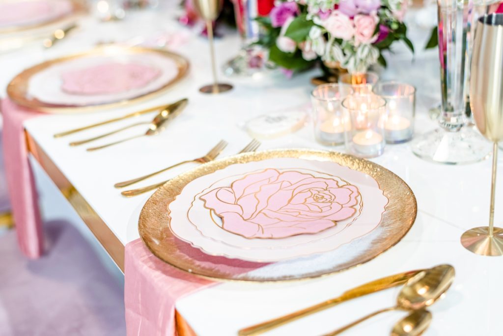 Luxury bridal shower table setting with gold chargers, gold silverware and pink flower plates.