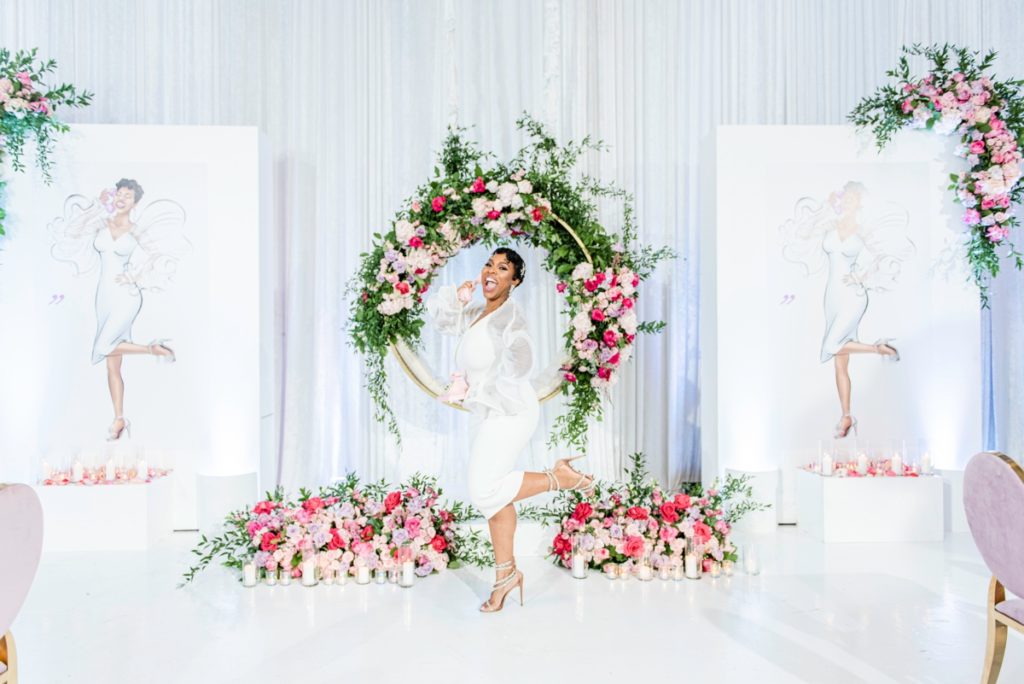 Bride standing in front of luxury pink floral arrangements and sketches of the bride to be.