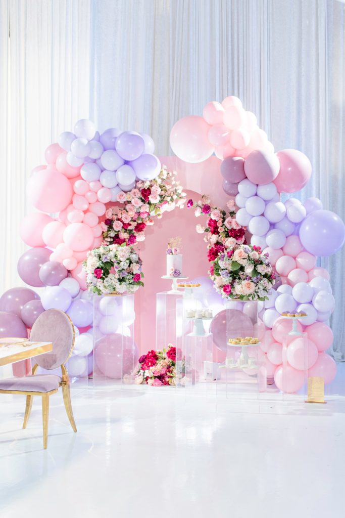 Luxury Bridal Shower cake display using acrylic cake stands, a ini flower arch and a punk and purple balloon arch.