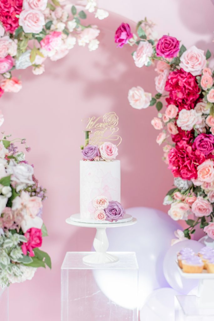 Luxe wedding cake display using a pink and white flower arch.