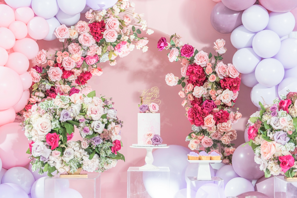 Luxe cake display using balloon arch and mini flower arch on a pink backdrop.