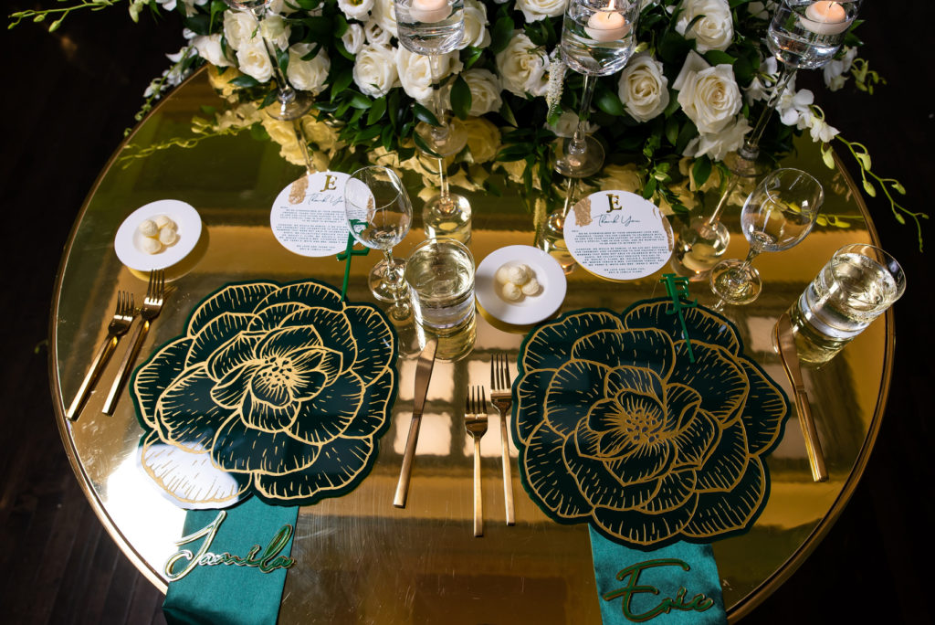 Black and gold flower cutout place mats with emerald green napkins and acrylic name place settings
