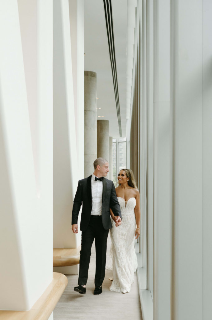 Bride and groom walking down a hallway with tall windows