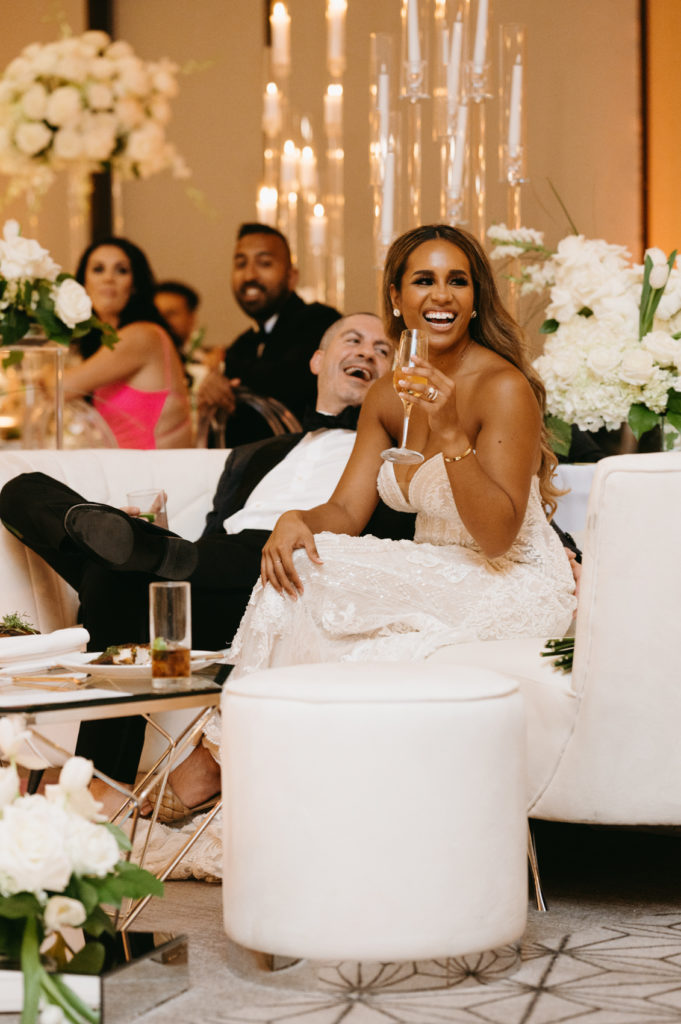 Bride and groom laughing while lounging at their white wedding reception
