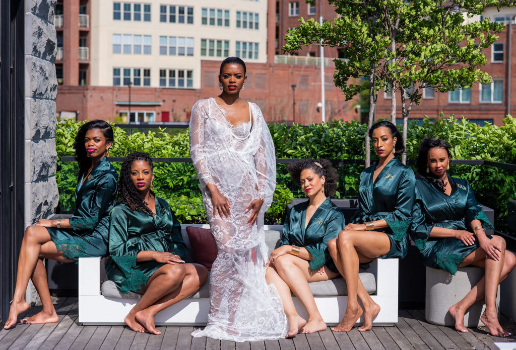 Boudoir shot of bride in a white lace robe and bridesmaids in emerald green robes