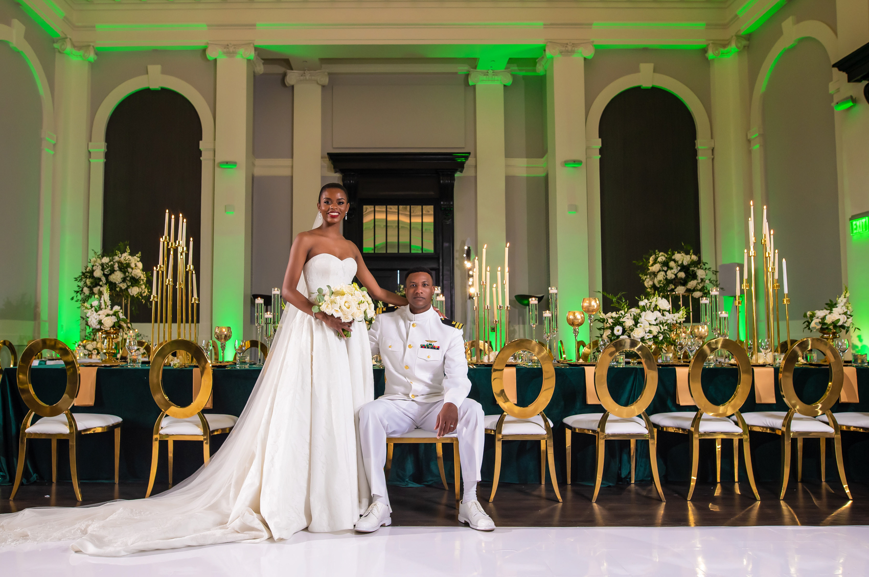 Bride and groom sitting at a long reception table with white flowers and gold chairs