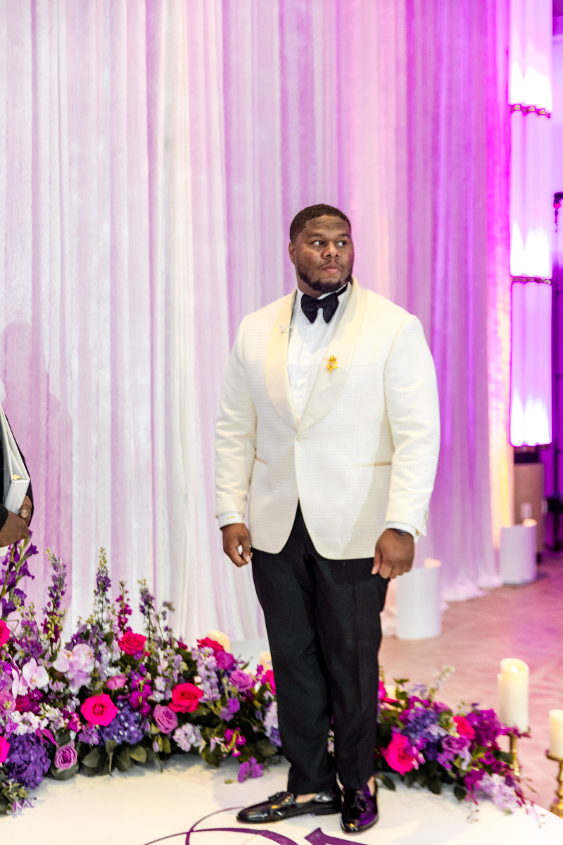 groom in white tuxedo with NOLA wedding colors for ceremony
