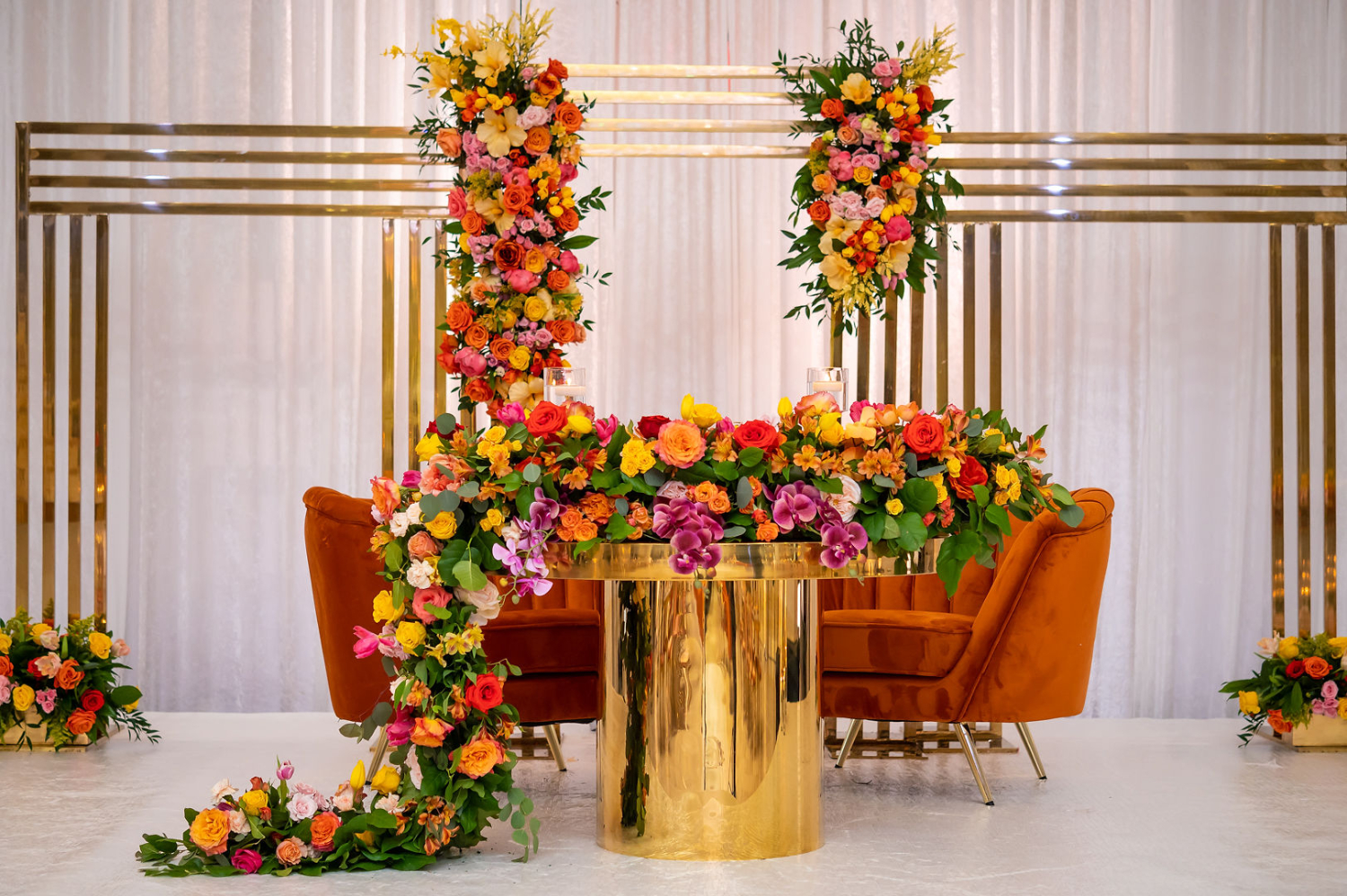 sweetheart table with orange velvet couch and cascading floral centerpieces