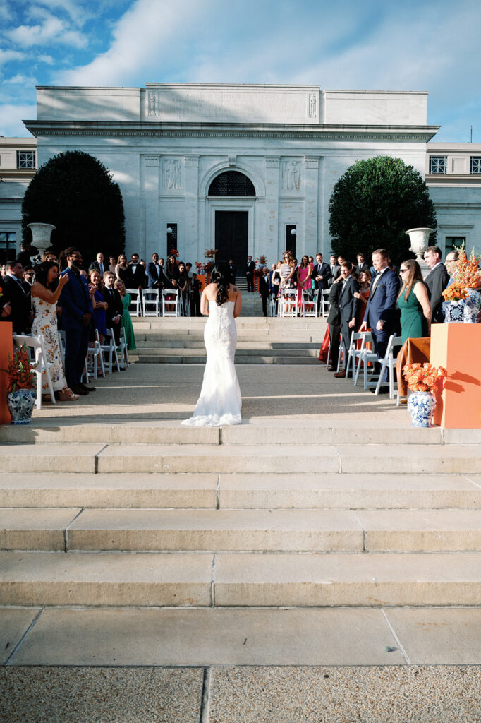 Bride walks down aisle toward her groom at the end of the aisle during this  Potomac View Terrace wedding.