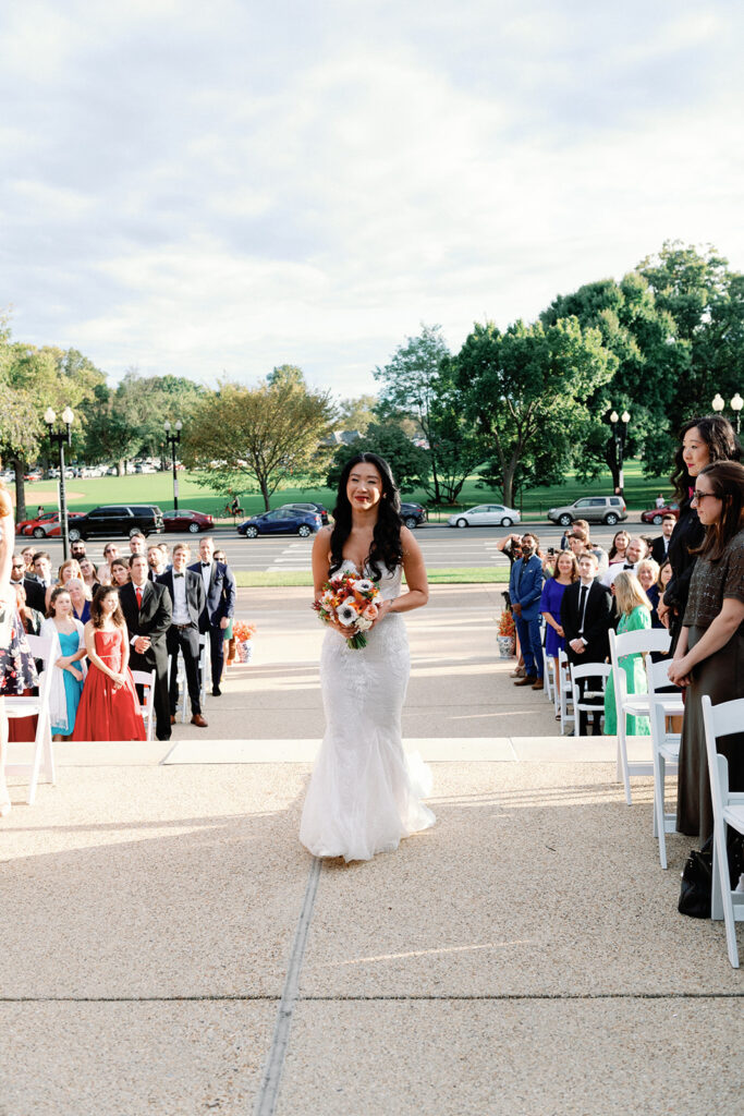 Bride walks down aisle toward her groom at the end of the aisle during this  Potomac View Terrace wedding.