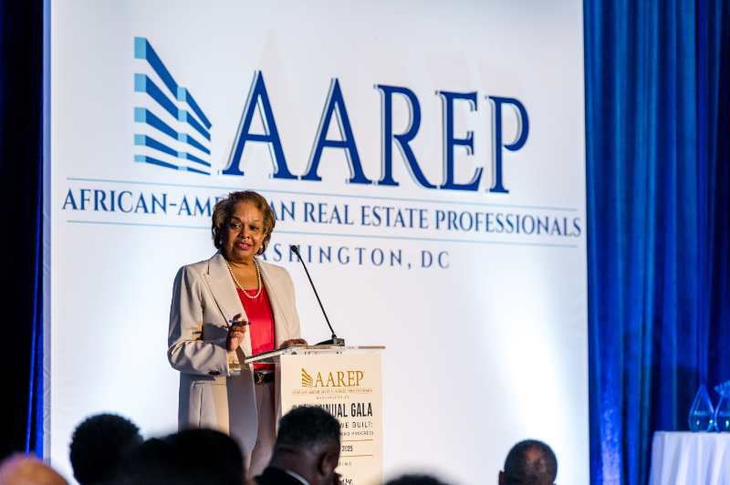 Woman in tan suite gives speech during AAREP gala.