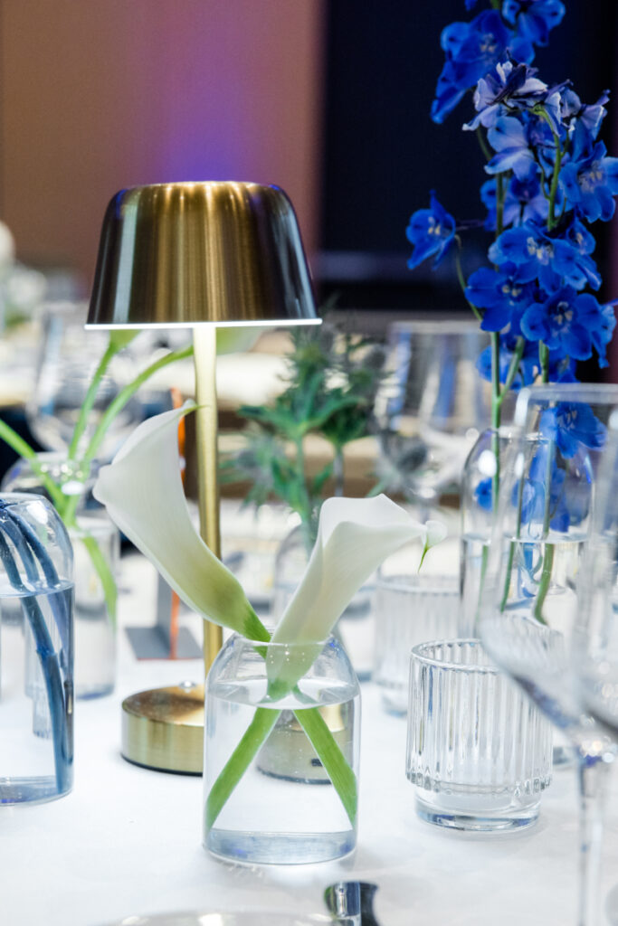 Bud vase with white flowers sitting on table setting.