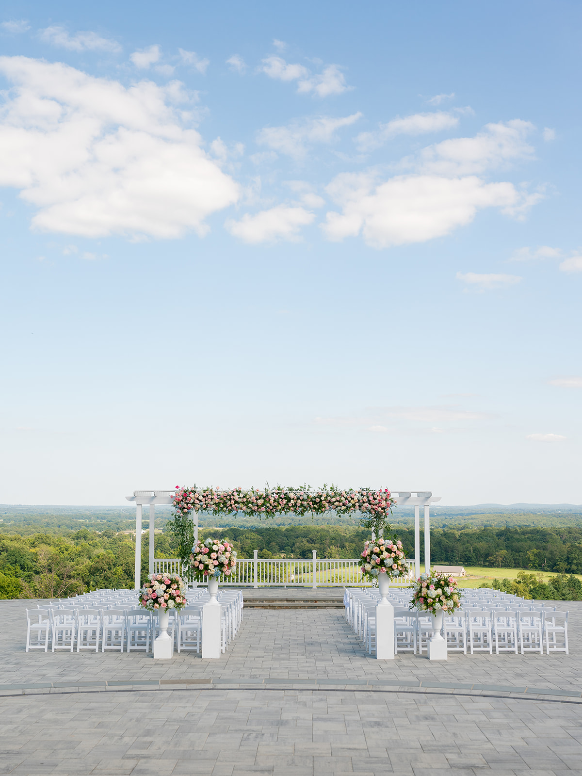 Ceremony setup for mansion wedding at the View of Bluemont with white chairs, white pedestals with large floral arrangements, and a pergola arranged with many florals.