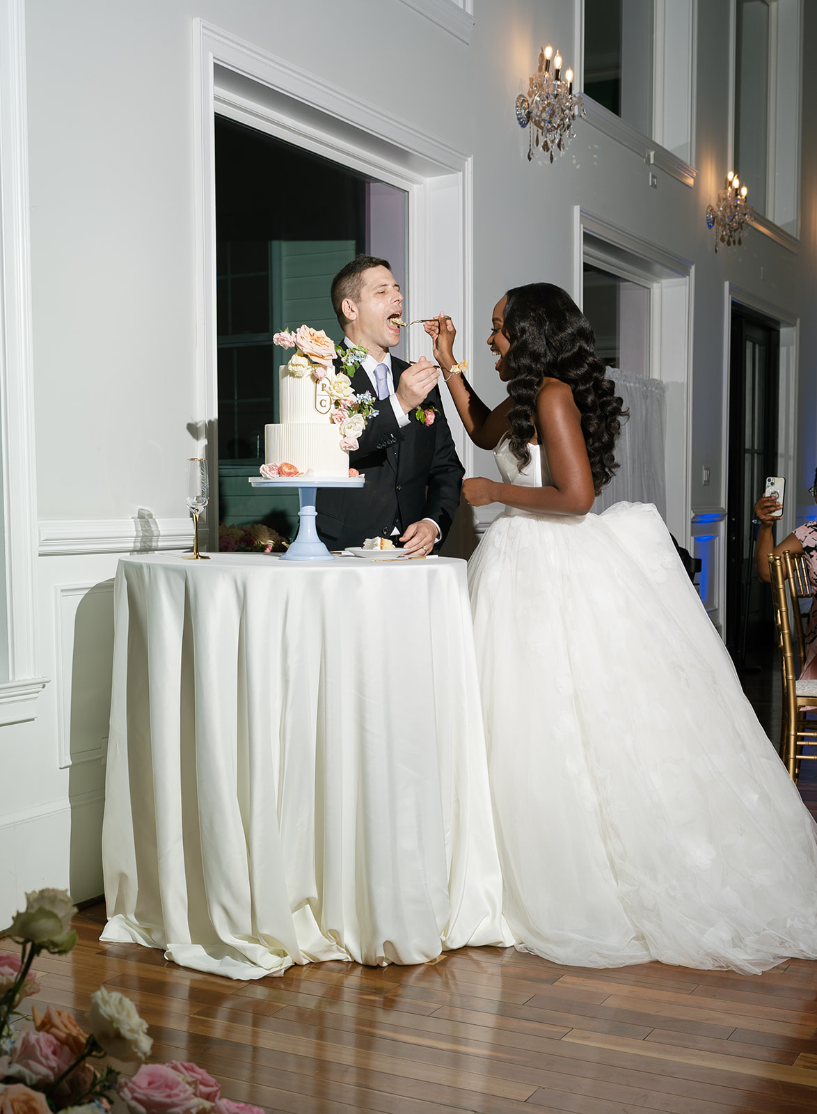 Bride feeds groom cake during cake cutting at wedding reception.