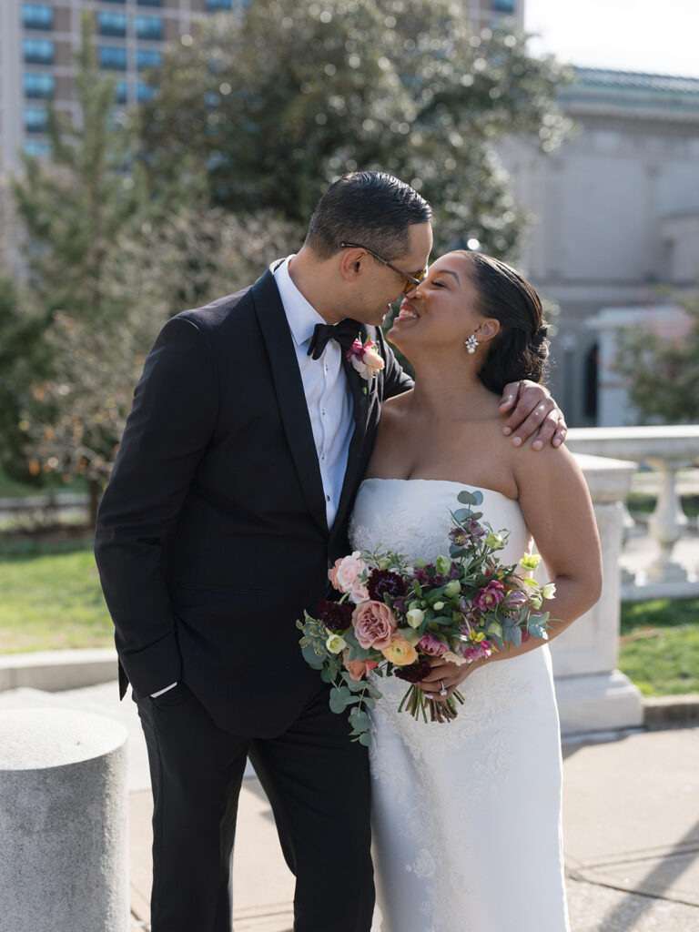 Bride and groom share a joyful embrace outdoors while the bride holds a colorful bouquet on their wedding day.