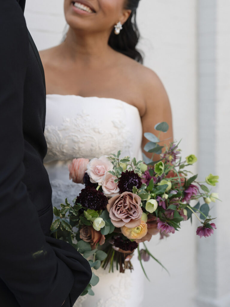 Close-up of the bride's lace wedding gown and colorful bouquet during outdoor portraits.