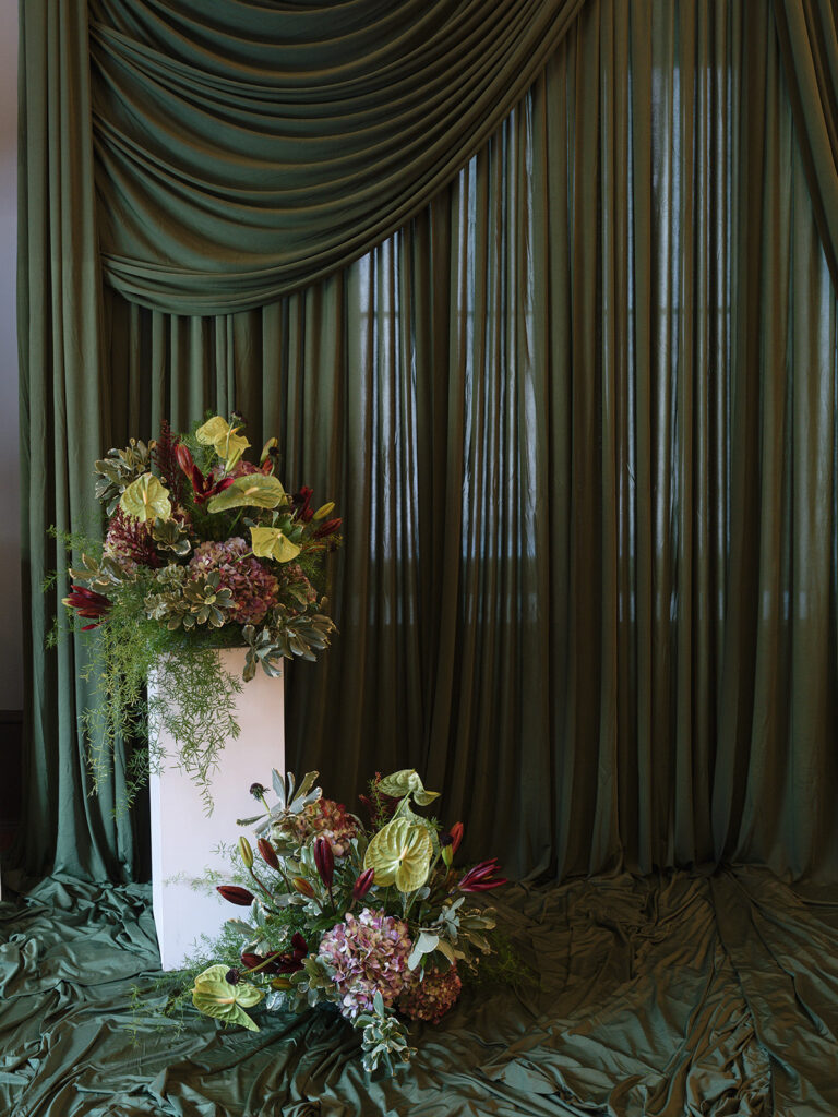 Floral ceremony arrangements displayed against green drapery at a historic library wedding venue.