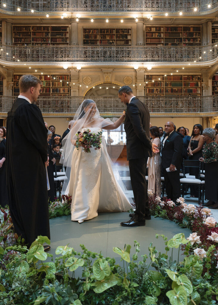 Bride greets the groom during their ceremony at a historic library wedding venue surrounded by family and friends.