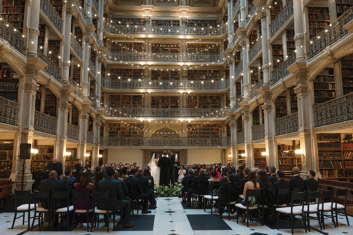 Historic library interior prepared for an elegant wedding ceremony with glowing string lights and towering bookshelves.