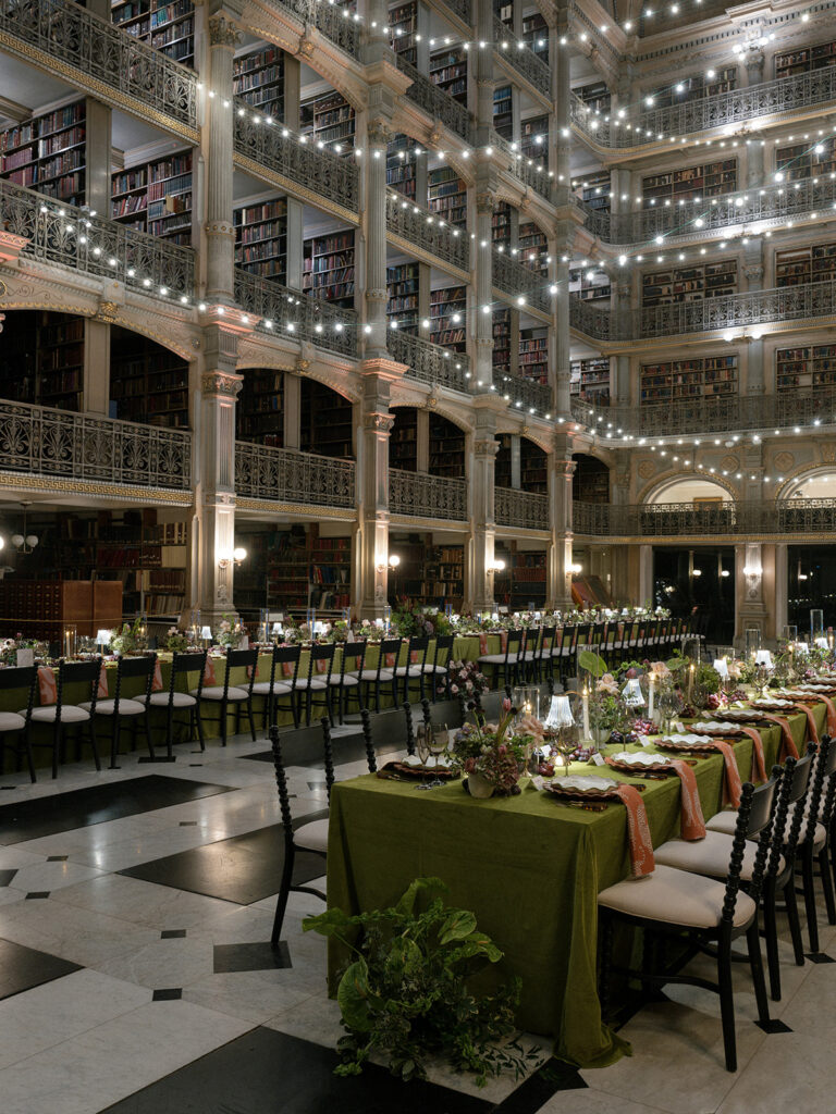 Reception tables with layered place settings beneath twinkling lights inside the historic George Peabody Library.