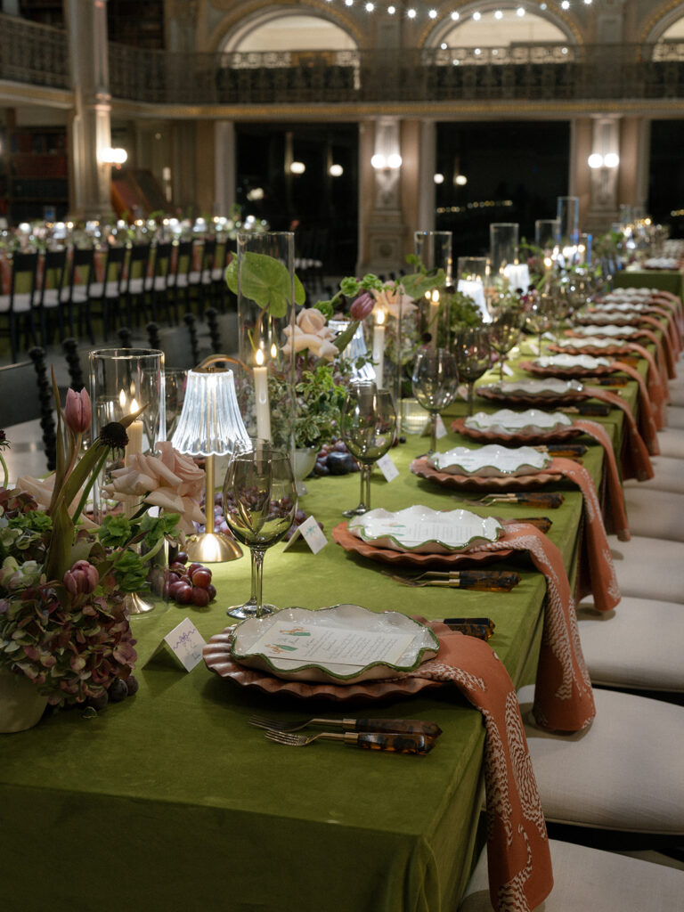 Long reception table with layered place settings, candlelight, florals, and custom details inside the George Peabody Library.