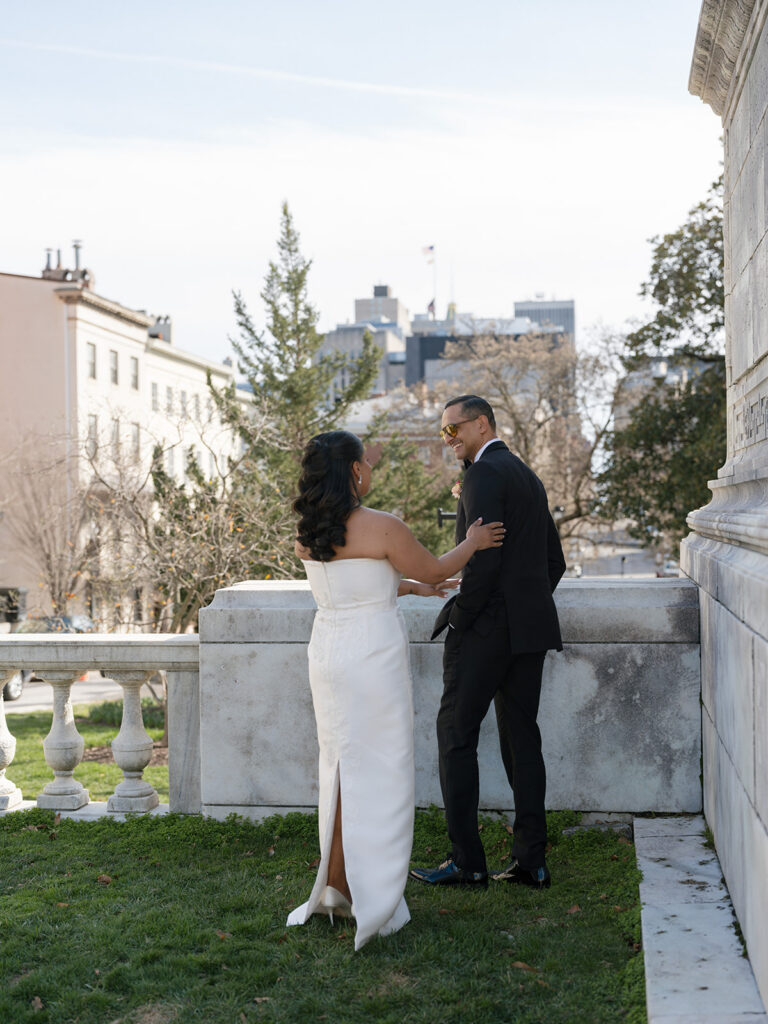 Bride playfully reaches for the groom during relaxed wedding portraits outside the historic venue.