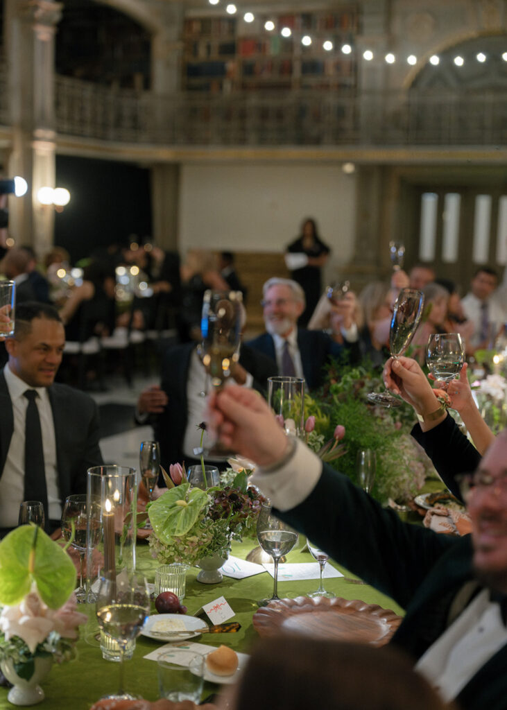 Wedding guests raise champagne glasses for a heartfelt toast during the couple's elegant library reception.
