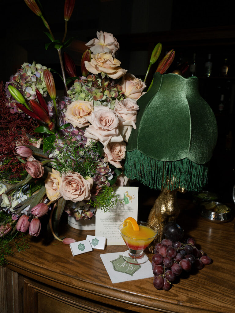 Signature cocktail displayed with grapes, lush florals, custom stationery, and vintage décor on the reception bar.