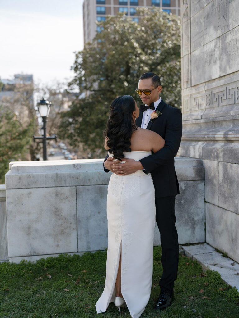 Bride and groom embrace during romantic wedding portraits beside the historic stone architecture.
